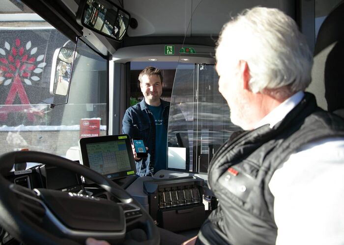 Mann begrüßt beim Einsteigen in den Bus den Busfahrer und zeigt sein Guest Mobility Ticket vor.