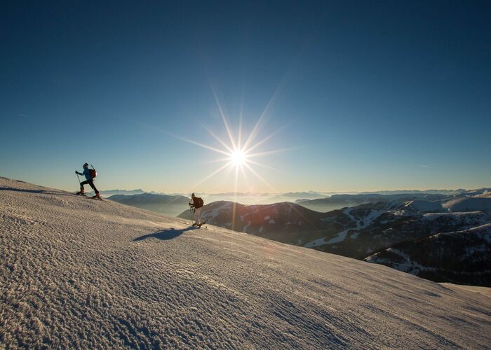 Zwei Skitourengeher steigen bei Sonnenaufgang durch die verschneiten Nockberge