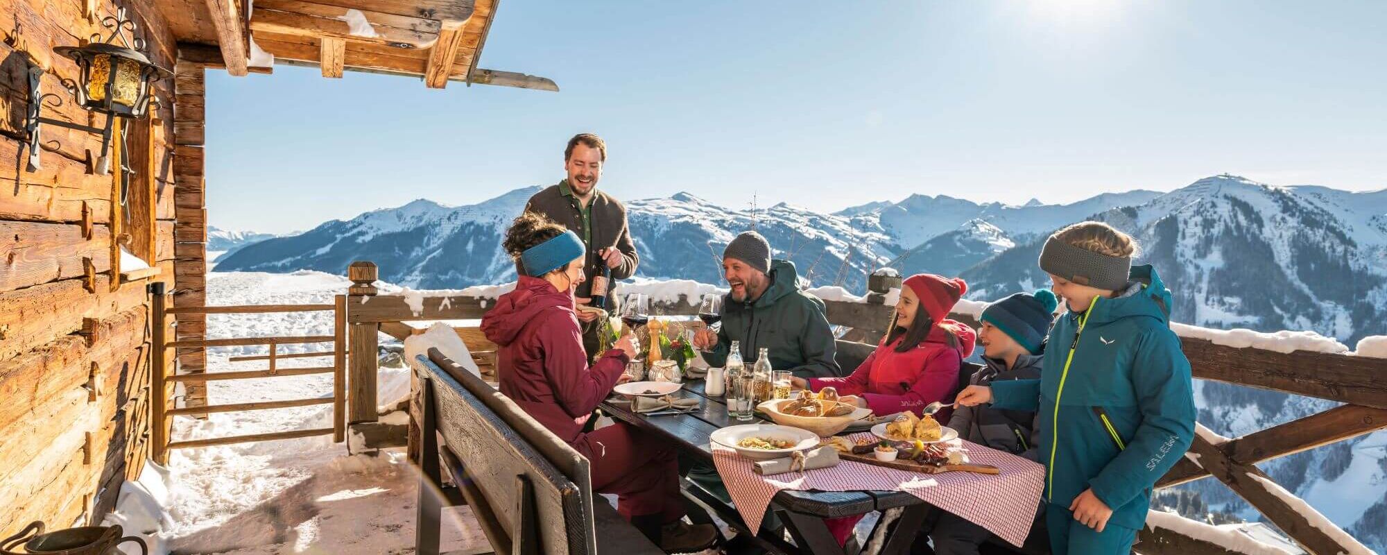 Familie im lustigen Gespräch mit dem Wirt auf der Terrasse einer Skihütte