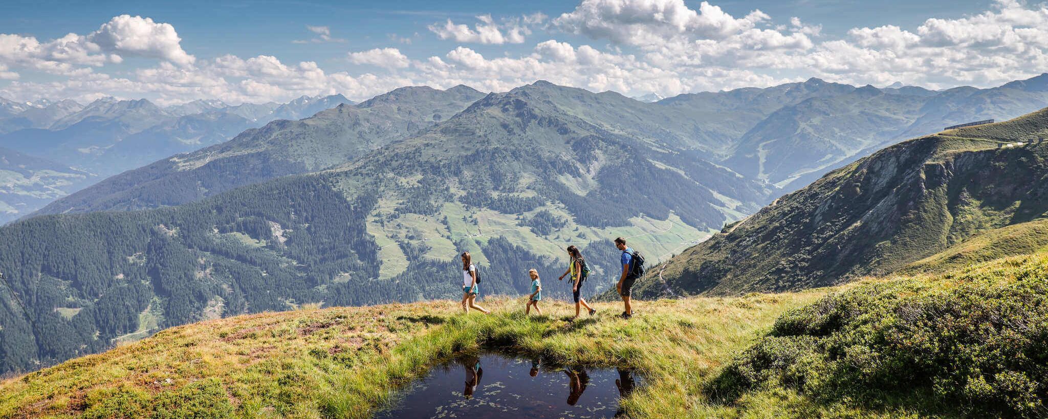 Een gezin wandelt in een hoogalpien landschap met groene berghellingen en panoramisch uitzicht op de Zillertaler Alpen