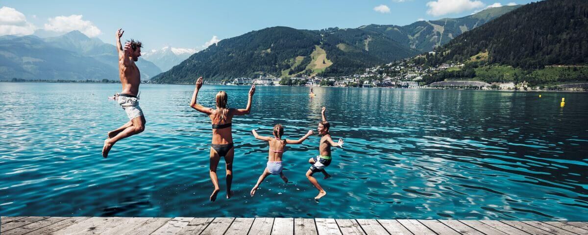 A family joyfully jumps into Zellersee's clear waters against a stunning mountain backdrop.