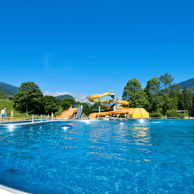 A vibrant swimming pool at Alpenbad Montafon features exciting water slides and scenic mountain views. | © Alpenbad Montafon