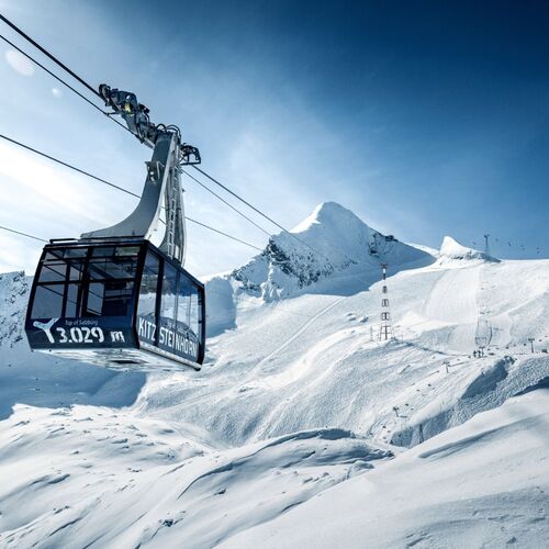 Die Kitzsteinhorn Gipfelbahn schwebt über verschneite Hänge bei strahlendem Himmel und majestätischen Bergen.