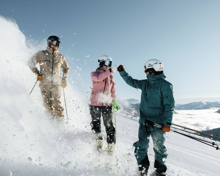 3 Skifahrer-Freunde stehen auf der Piste und geben sich ein High Five.