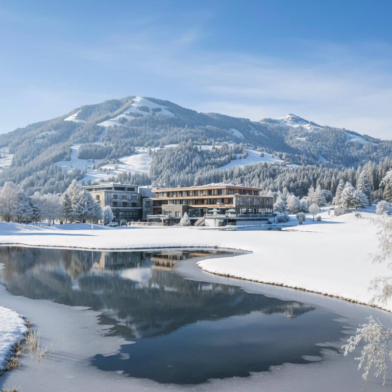 Bergresort Westendorf hinter einem verschneiten Teich mit Bergen und Raureif-Bäumen