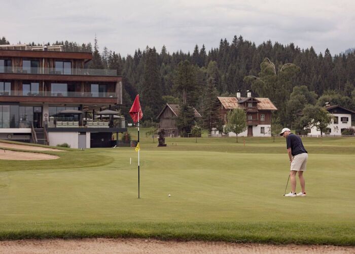 Een golfer putt op de groene fairway van een golfbaan in Westendorf, omringd door bossen en gebouwen.