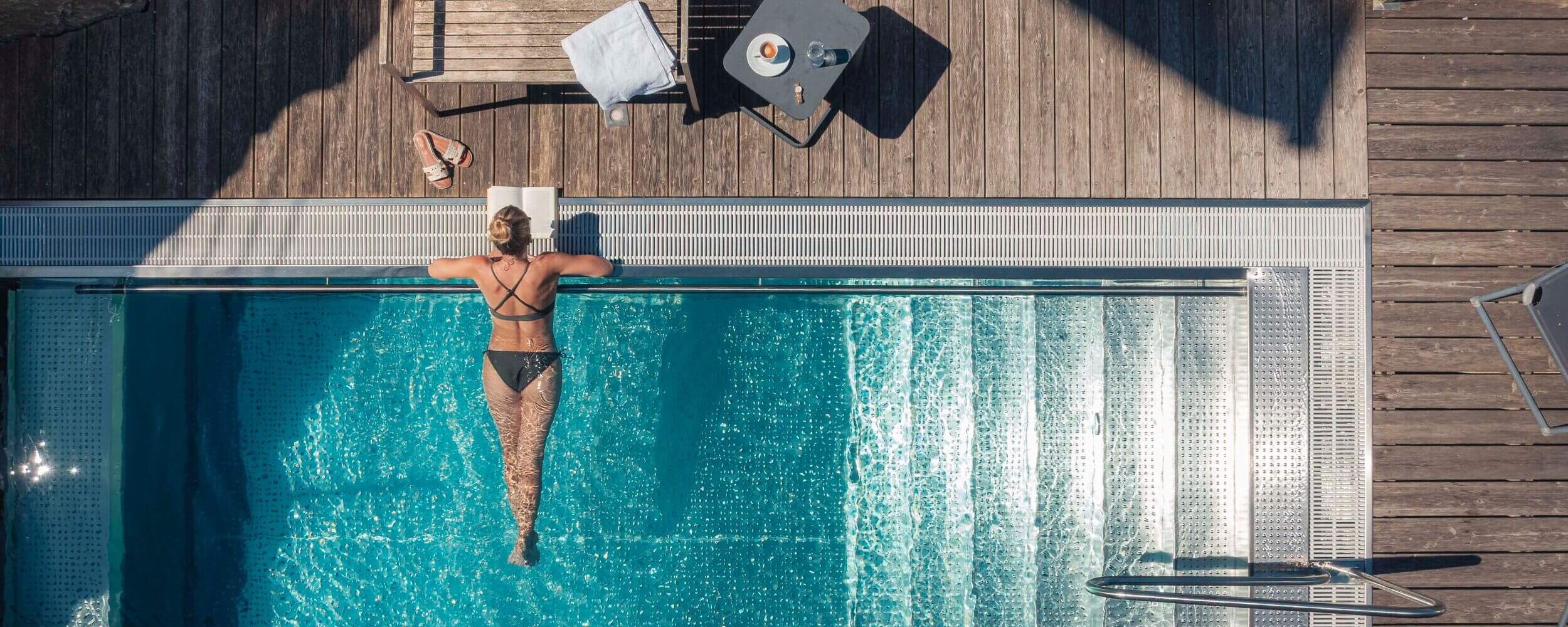 Jonge vrouw ligt alleen in het zwembad van haar privé vakantiehuis en leest een boek.