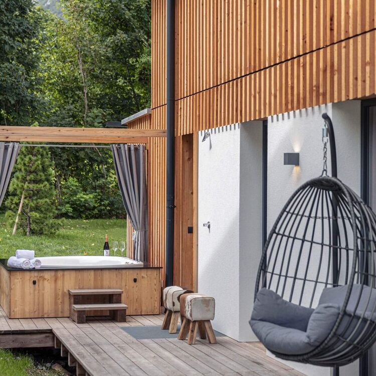 Ein modernes Haus mit einem Holz-Whirlpool und einem gemütlichen Schwebesessel in einer grünen Umgebung.