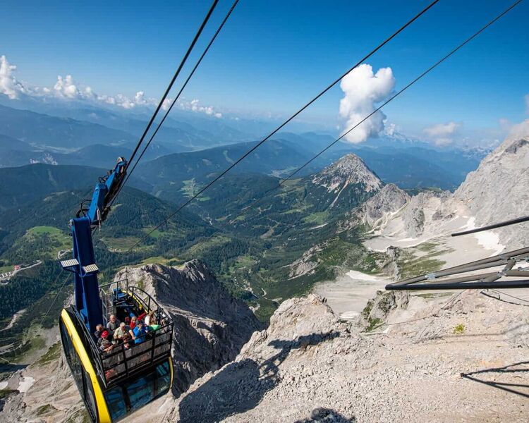 A panoramic gondola ascends the Dachstein Glacier, offering stunning views of the mountains and green valleys below.