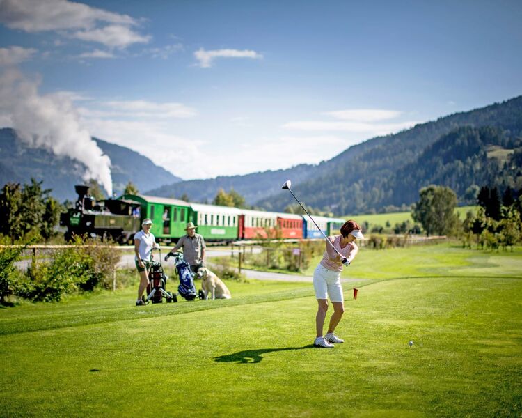 Golferin am Golfplatz, im Hintergrund die Murtalbahn
