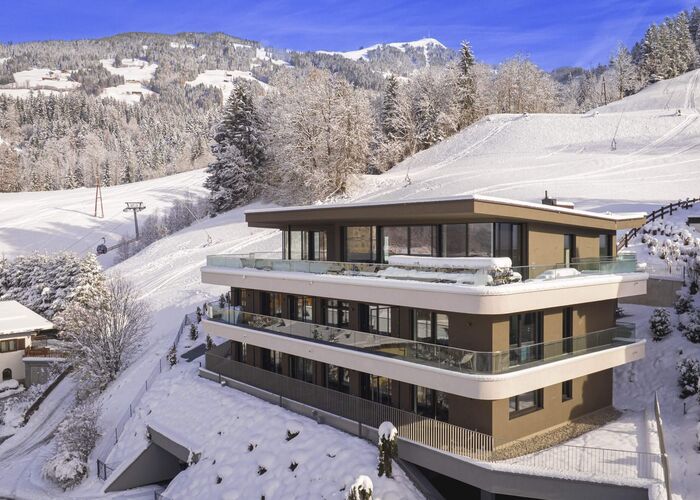 Modernes Gebäude im Winter mit schneebedeckten Bergen und Skigebieten in der Umgebung.