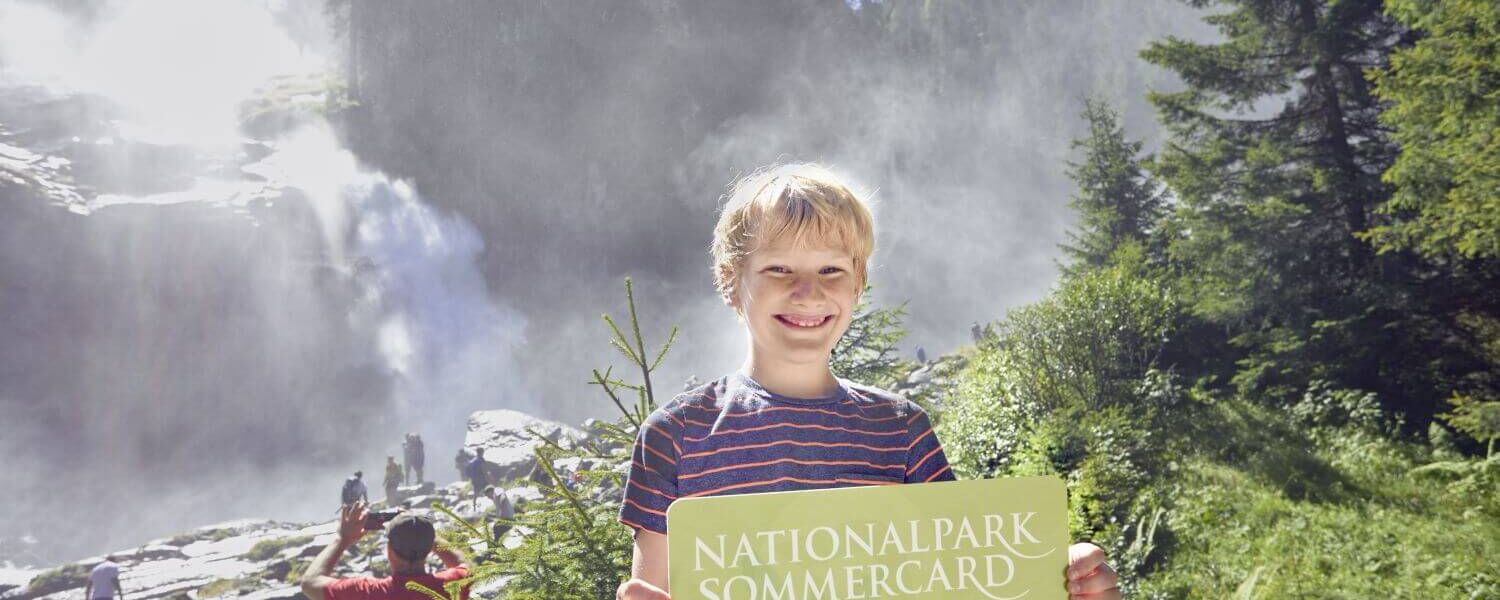Junge vor den Krimmler Wasserfälle hält die Nationalpark Sommercard in der Hand