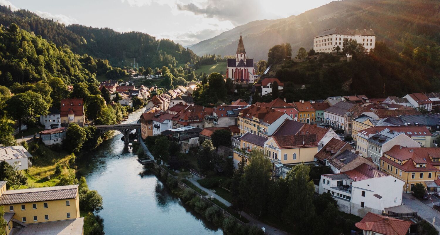 Blick von oben auf die historische Altstadt von Murau in der Steiermark, umgeben von alpiner Landschaft.