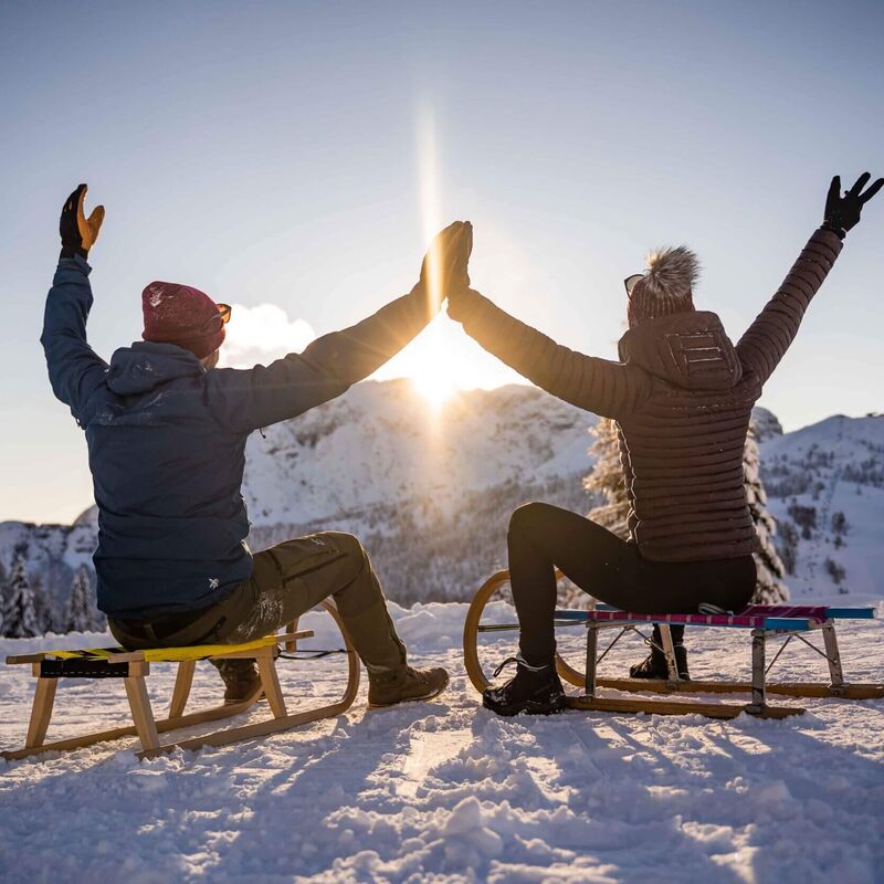 Menschen beim Rodeln auf einer verschneiten Bahn am Nassfeld mit winterlicher Bergkulisse