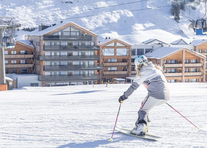Skiërs op de besneeuwde piste in Rauris met Carpe Solem Rauris en het winterse berglandschap op de achtergrond.