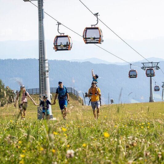 Familie beim Wandern am Kreischberg mit Sommerbergbahn im Hintergrund.