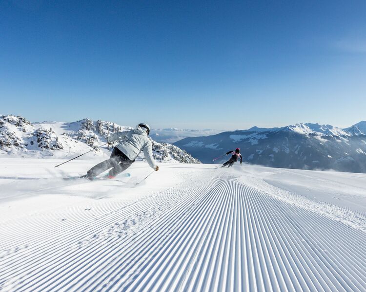 Skiers carve through fresh powder on pristine slopes at Hochzillertal, surrounded by majestic mountains.
