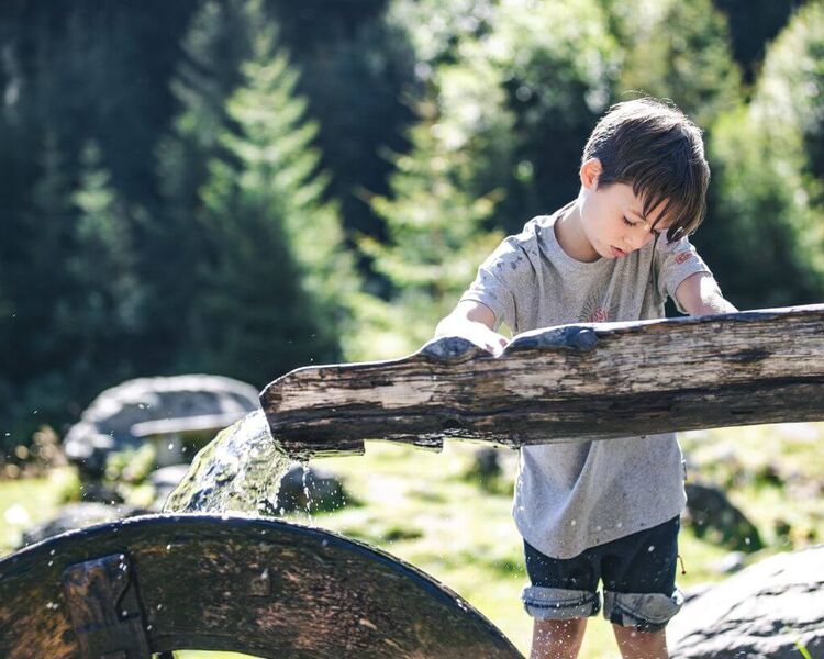 A child examines a wooden water wheel.