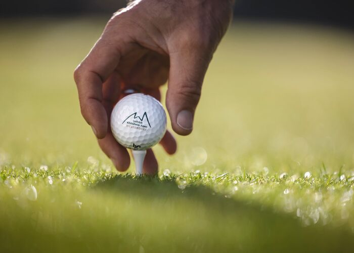 Eine Hand platziert einen Golfball sanft auf dem grünen Gras im Golfclub Kitzbüheler Alpen.
