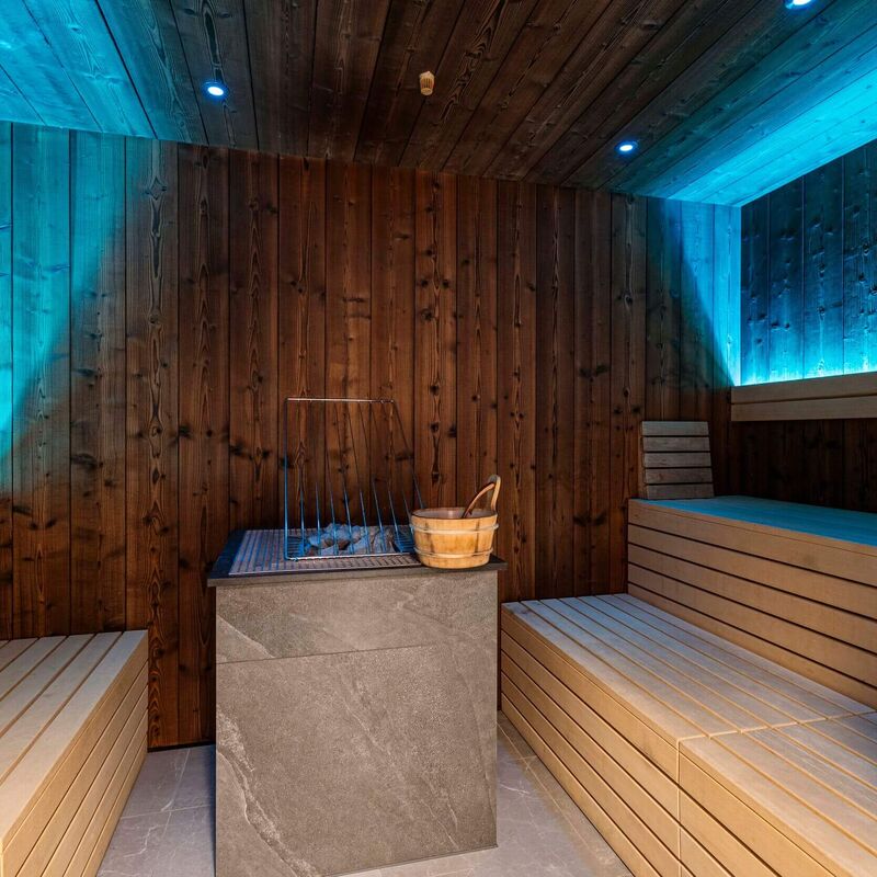 Sauna with cosy wooden benches, stone sauna heater and relaxing lighting by ALPS RESORTS