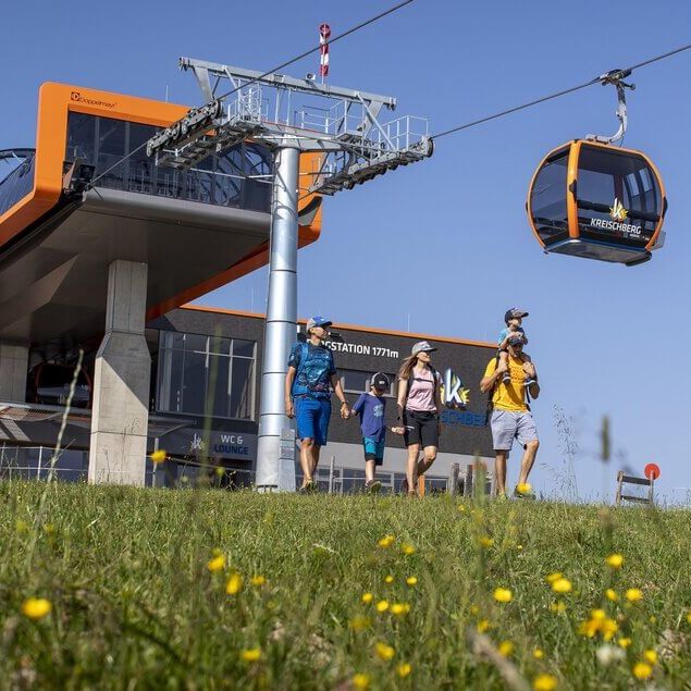 Family hiking at Kreischberg with the summer cable car in the background.