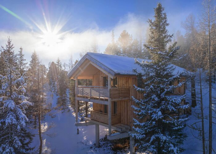 Außenansicht eines Chalets der Naturchalets Turracher Höhe im Winter, umgeben von schneebedeckten Bäumen und der winterlichen Natur der Nockberge.