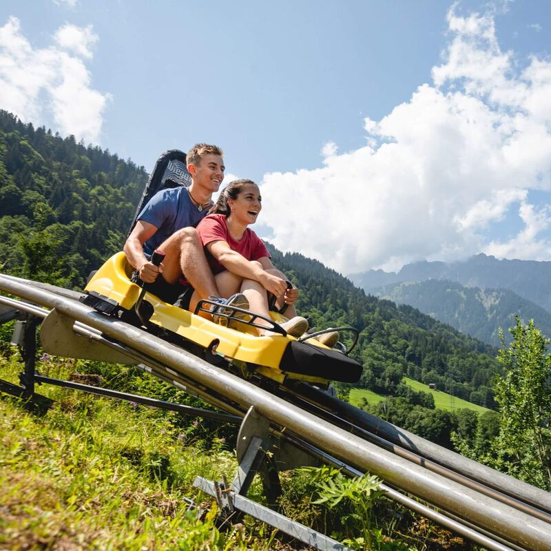 Ein Paar genießt eine Fahrt auf der Sommer-Alpenachterbahn in den Bergen bei strahlendem Sonnenschein. | © Stefan Kothner