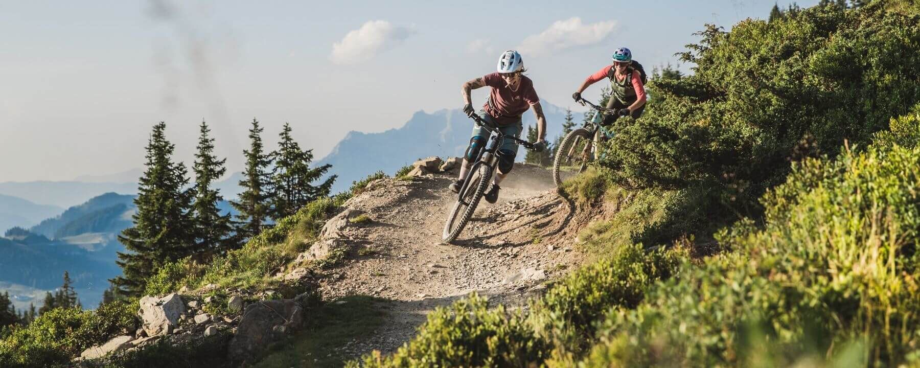 Twee downhillbikers razen over een alpien parcours, omringd door indrukwekkend berglandschap