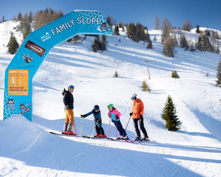 Eine Familie steht an der Familienpiste, bereit zum Skifahren in der verschneiten Berglandschaft.