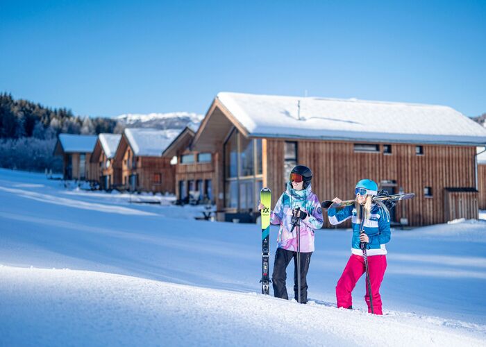 Two skiers stand in snowy terrain near cozy Kreischberg Chalets, ready for an adventurous day on the slopes.