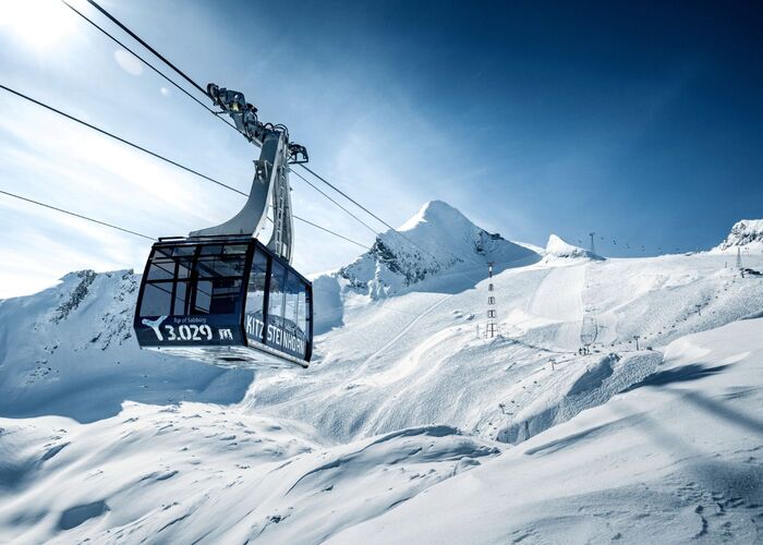 Een kabelbaan stijgt naar de top van de Kitzsteinhorn, omringd door sneeuwbedekte bergen en een heldere lucht.
