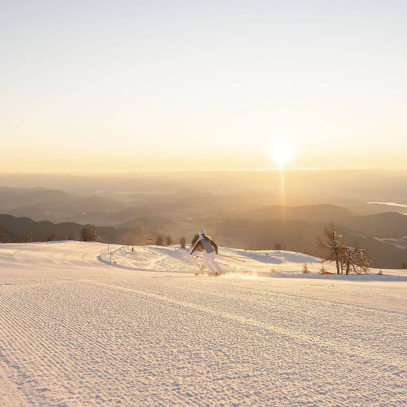 Eine Skifahrerin fährt über die breite Skipiste der Gerlitzen Alpe, umgeben von einem beeindruckenden Panorama.