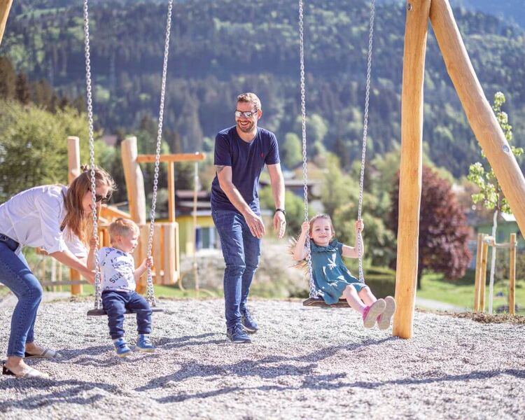 Jungfamilie auf einem Spielplatz mit 2 schaukelnden kleinen Kindern