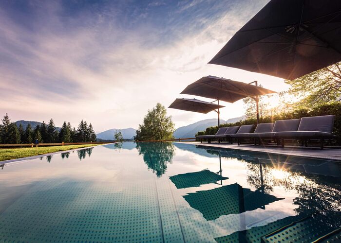 Außenpool im Hideaway Dachstein West mit Liegen, Sonnenschirmen und Blick auf die Berge in der Abendsonne.
