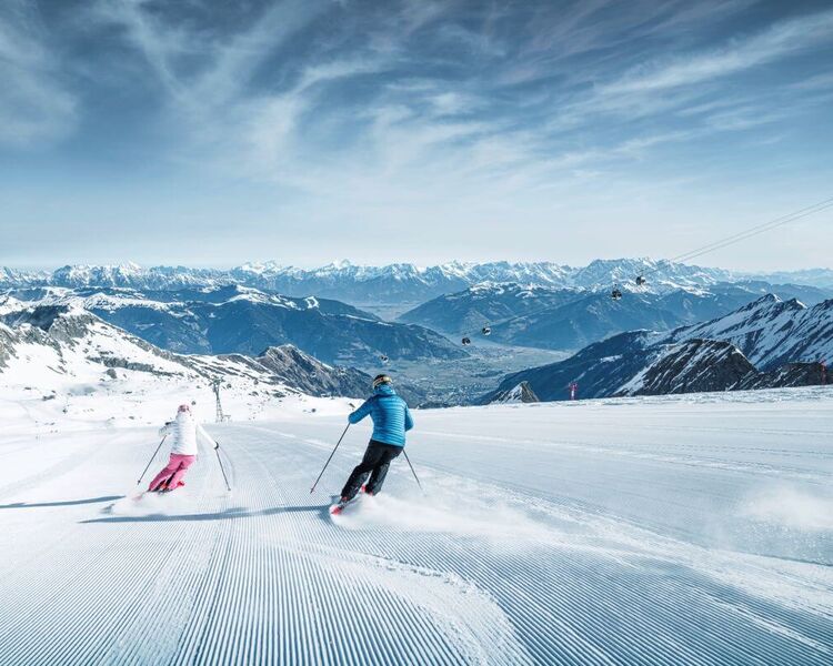 2 Skifahrer am Gletscher, im frühlingshaften Tal sieht man den Zeller See.