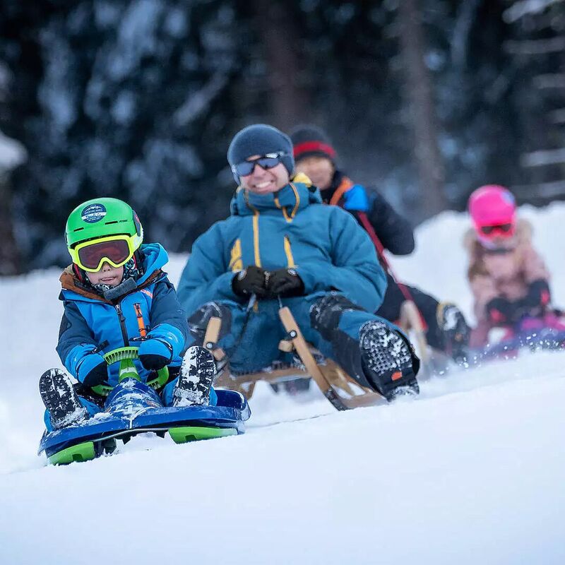 Familie rodeln fröhlich im Raurisertal auf einer verschneiten Piste | © TVB Rauris