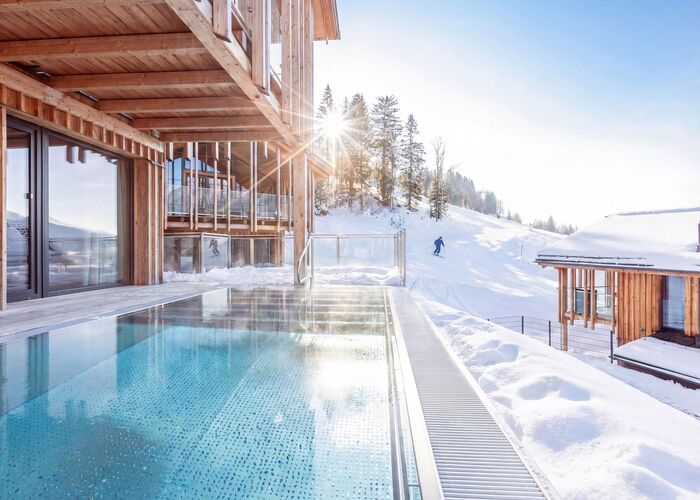 A stunning poolside view at a Schladming chalet, with snow-covered slopes and sunlight shining through the trees.