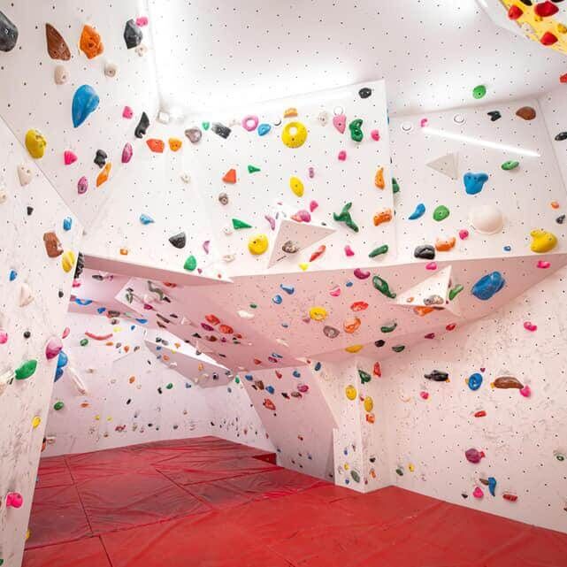 Indoor-Boulderraum mit bunten Klettergriffen, überhängenden Wänden und roten Fallschutzmatten