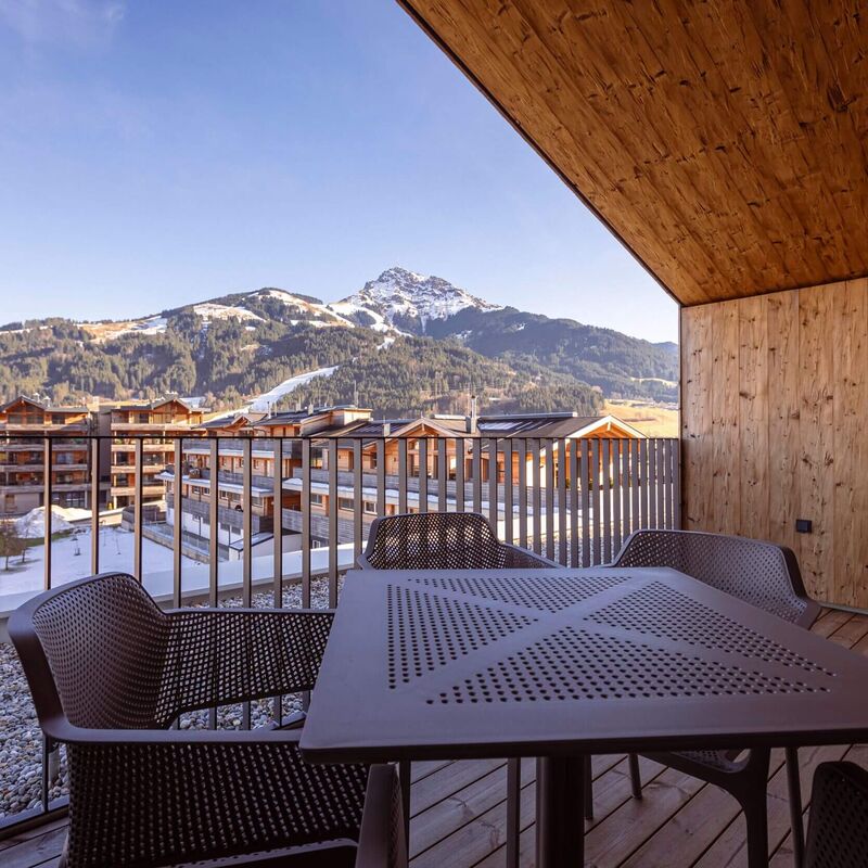 A balcony with a table overlooks snow covered mountains and wooden buildings in a serene winter landscape.