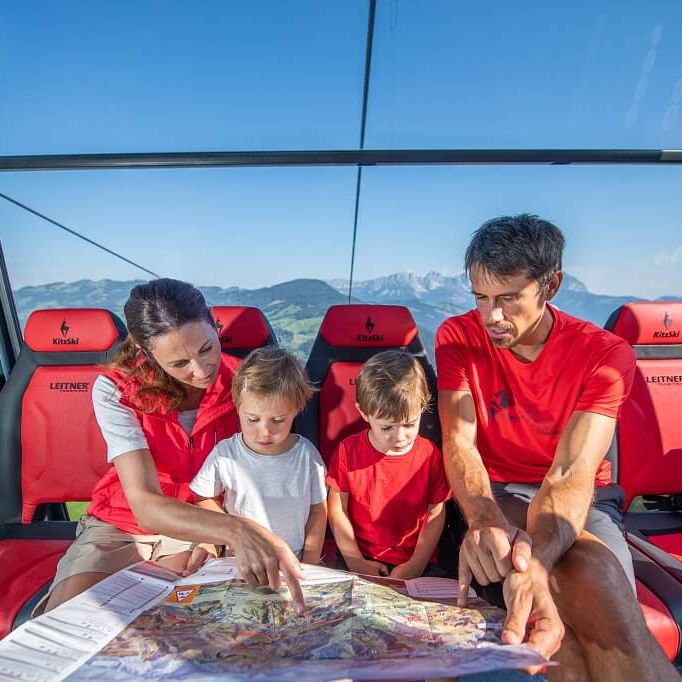Family with 2 children sitting in a glazed gondola and studying the hiking map.