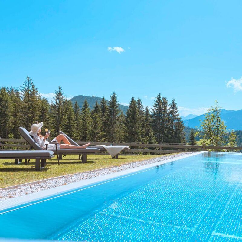 Junge Frau mit Sonnenhut genießt den Bergblick am Pool.
