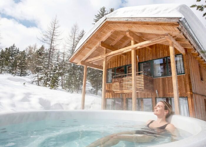 Een vrouw ontspant in een warmwaterbad bij een houten chalet in de besneeuwde Alpen.