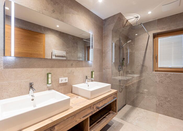 Twee wastafels, een grote spiegel en een douchecabine in een badkamer met een moderne feel good stijl