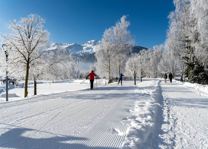 Langlaufende Personen gleiten durch verschneite Landschaft mit Bäumen im Winter hinter dem TVB Uttendorf.