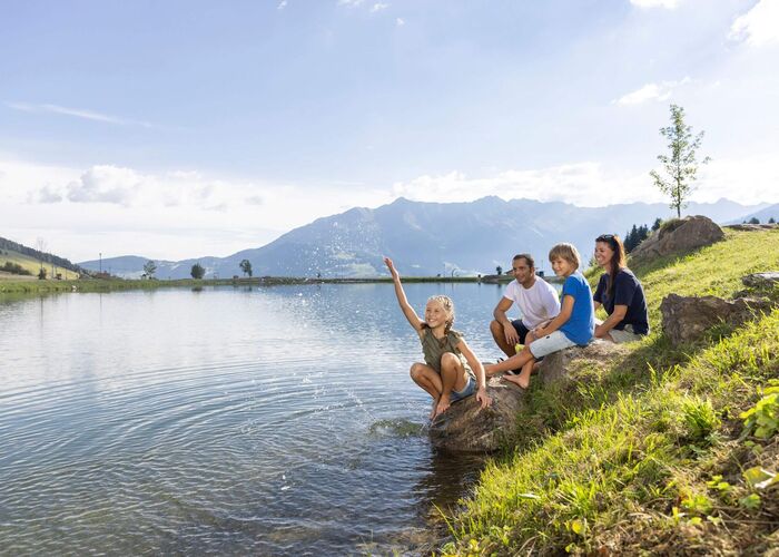 Familie ontspant bij de Wolfsee, kinderen spelen met water, omgeven door groene natuur en uitzicht op de bergen