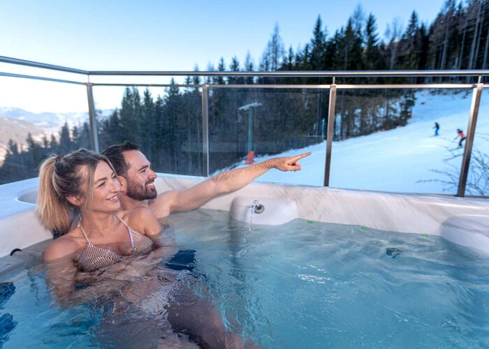 Pärchen relaxed gemütlich im Jacuzzi mit Ausblick auf die Skipiste