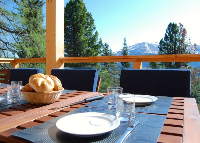 Vers gedekte ontbijttafel op een zonnig terras met uitzicht op groene berghellingen en met sneeuw bedekte alpentoppen