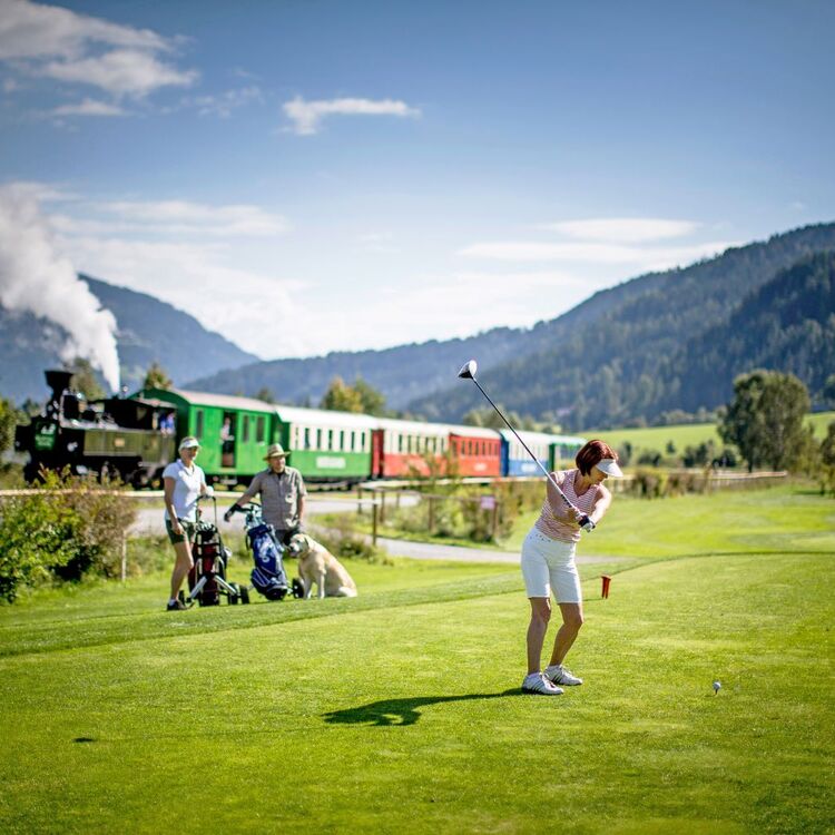 Golferin am Golfplatz, im Hintergrund die Murtalbahn