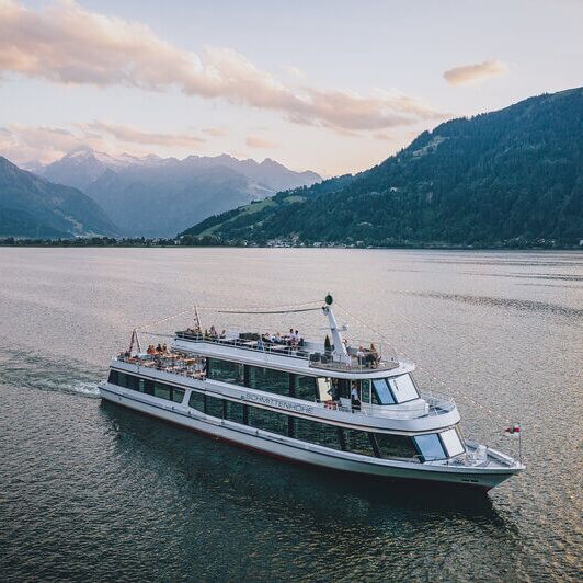 Schiff MS Schmitten fährt am Zeller See, umgeben von Bergen und Gletscher.