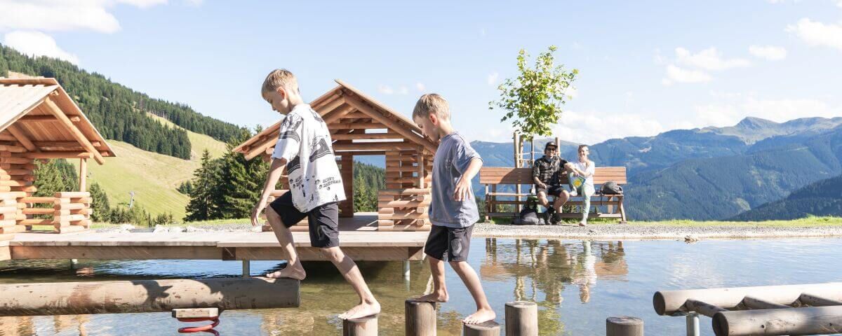 2 Kinder balancieren über Holzelemente im Wasser.